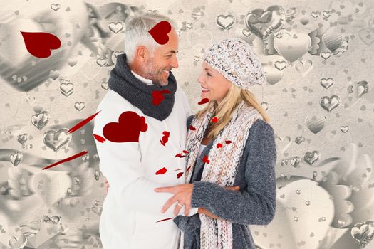 Happy couple in winter fashion embracing against grey valentines heart pattern