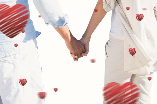 Couple on the beach looking out to sea holding hands against hearts