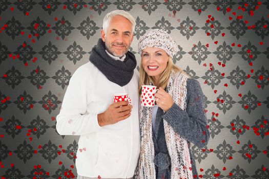 Happy couple in winter fashion holding mugs against grey wallpaper