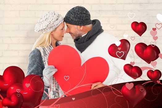 Smiling couple in winter fashion posing with heart shape against white wall