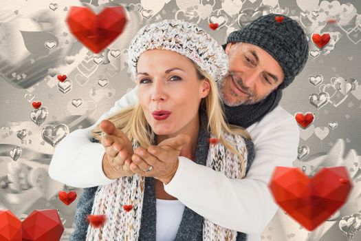 Smiling couple in winter fashion posing against grey valentines heart pattern