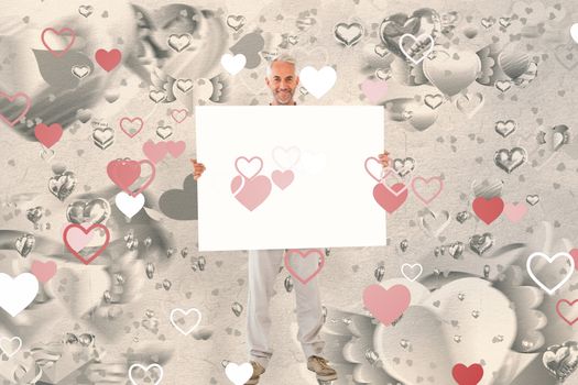 Smiling man showing large poster against grey valentines heart pattern