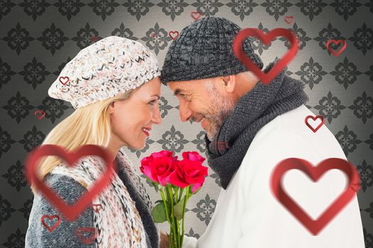 Smiling couple in winter fashion posing with roses against grey wallpaper