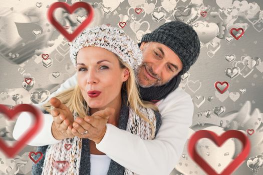 Smiling couple in winter fashion posing against grey valentines heart pattern