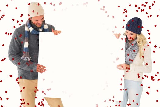 Attractive couple in winter fashion showing poster against red love hearts