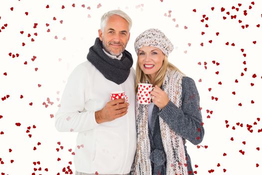 Happy couple in winter fashion holding mugs against red love hearts