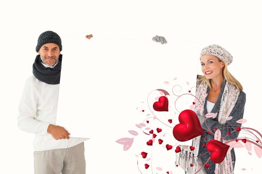 Smiling couple in winter fashion holding poster against valentines heart design