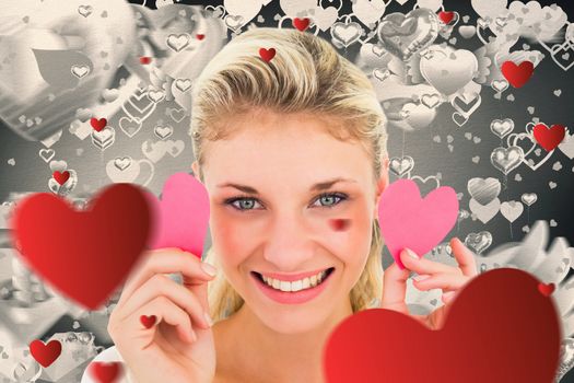 Attractive young blonde holding little hearts  against grey valentines heart pattern