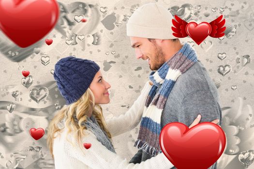 Attractive couple in winter fashion hugging against grey valentines heart pattern