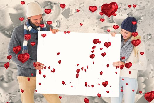 Attractive couple in winter fashion showing poster against grey valentines heart pattern