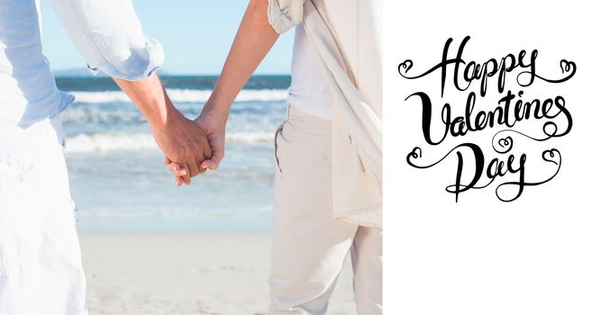 Couple on the beach looking out to sea holding hands against happy valentines day