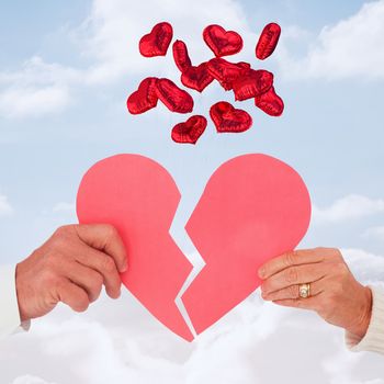 Couple holding a broken paper heart against cloudy sky