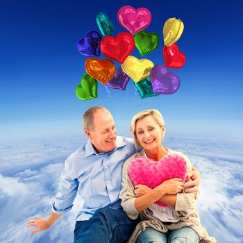 Happy mature couple with heart pillow against mountain peak through the clouds