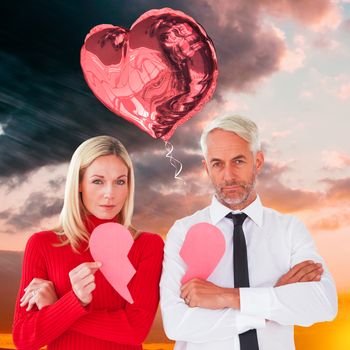 Couple not talking holding two halves of broken heart against orange and blue sky with clouds