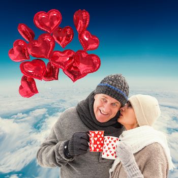 Happy mature couple in winter clothes holding mugs against blue sky over white clouds