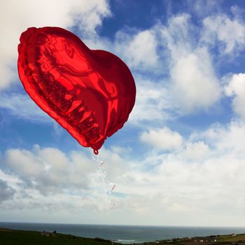 Red heart balloon against blue sky with white clouds