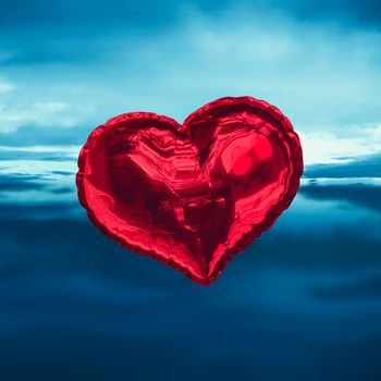 Red heart balloon against blue sky with blue clouds