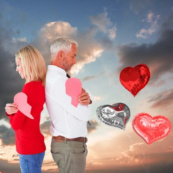 Couple holding two halves of broken heart against blue and orange sky with clouds