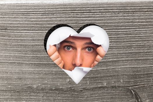 Young man looking through paper rip against heart in wood