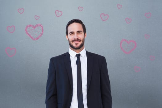 Smiling businessman in suit standing with hands in pockets against grey