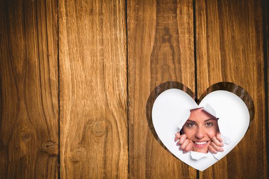 Young woman looking through paper rip against heart in wood