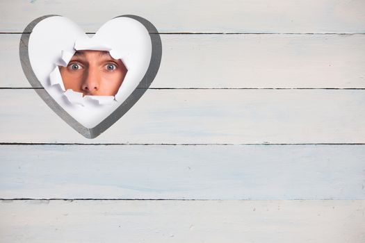 Young man looking through paper rip against heart in wood