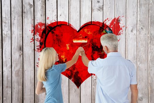 Happy couple painting wall with roller against paint splattered paper