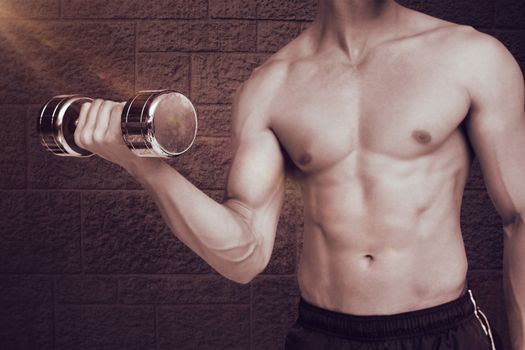 Fit shirtless man lifting dumbbell  against grey brick wall