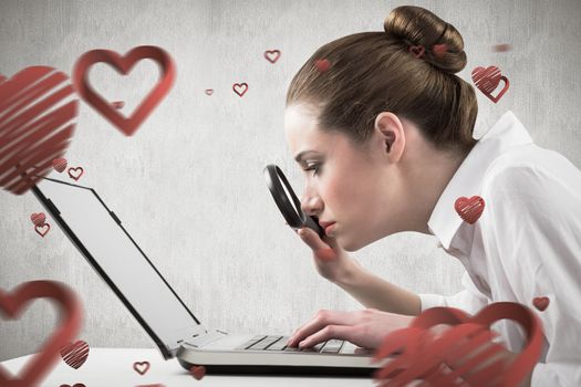 Businesswoman typing and looking through magnifying glass against white and grey background