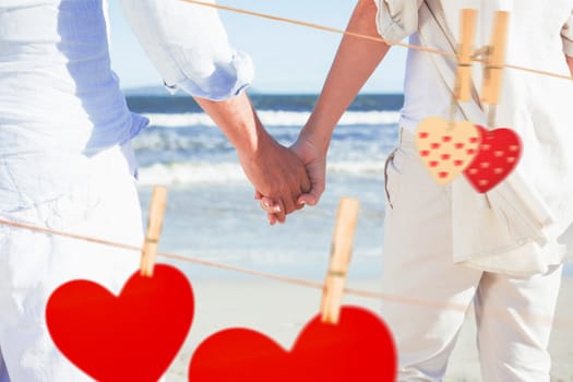 Couple on the beach looking out to sea holding hands against hearts hanging on the line