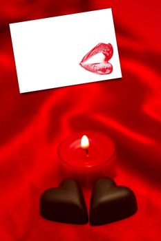 Chocolate hearts and lit candle against white card