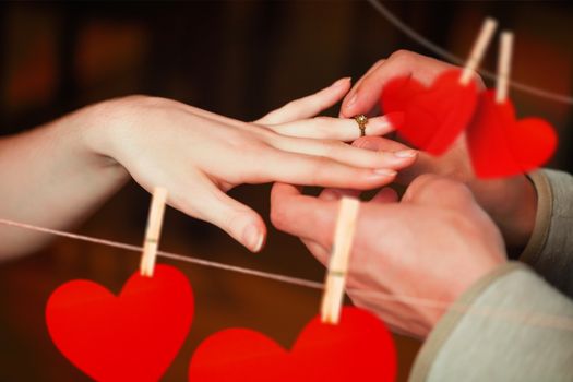 Close up on man putting on ring during marriage proposal against hearts hanging on a line