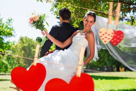 Newlywed couple sitting on scooter in park against hearts hanging on the line