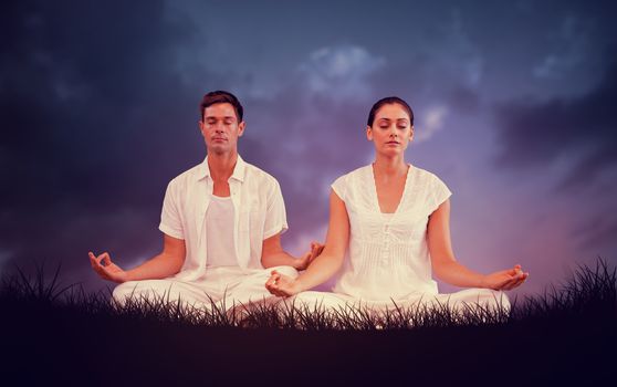 Attractive couple in white meditating in lotus pose against blue sky over grass