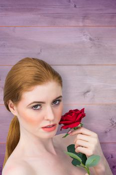 Beautiful redhead posing with red rose against wooden background in purple