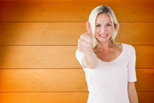 Happy blonde showing thumbs up and smiling at camera against wooden planks background