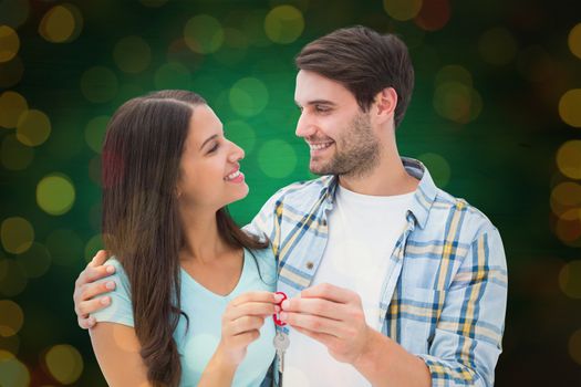 Happy young couple holding new house key against close up of christmas lights