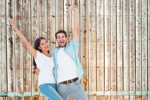 Happy casual couple cheering together against faded pine wooden planks