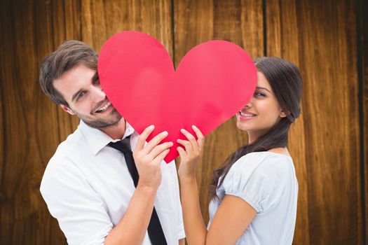 Couple smiling at camera holding a heart against wooden table