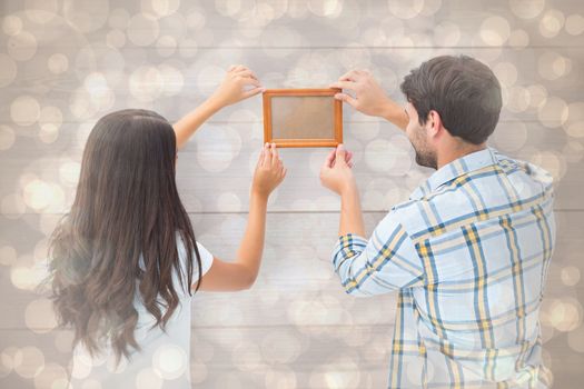 Happy young couple putting up picture frame against light glowing dots design pattern