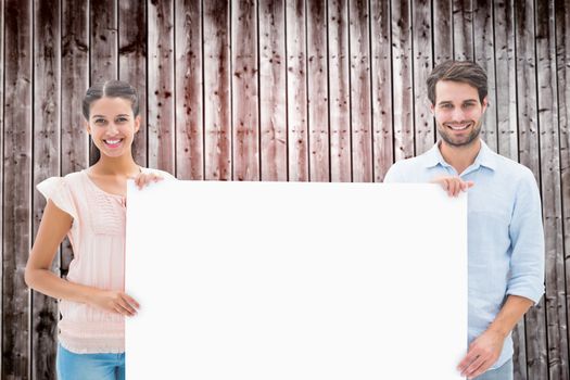 Attractive young couple smiling at camera holding poster against wooden planks