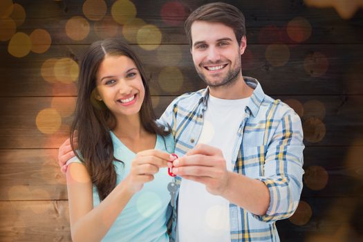 Happy young couple showing new house key against close up of christmas lights