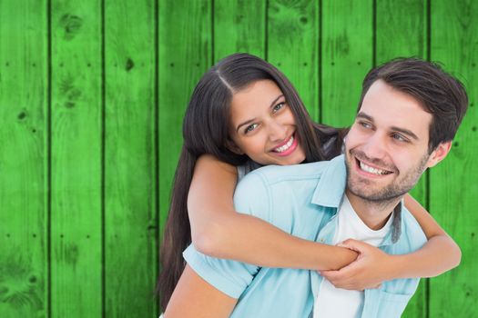 Happy casual man giving pretty girlfriend piggy back against bright green wooden planks