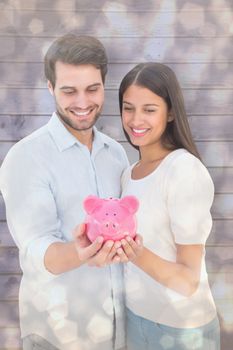 Happy couple holding their piggy bank against light glowing dots design pattern