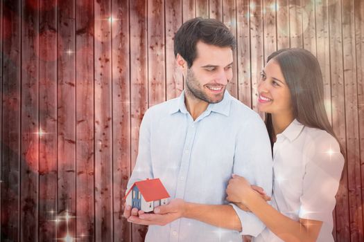 Attractive young couple holding a model house against light design shimmering on red