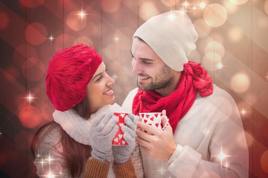 Winter couple holding mugs against light design shimmering on red