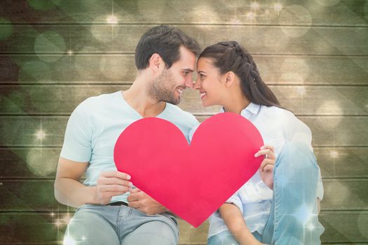 Cute couple sitting holding red heart against light design shimmering on green