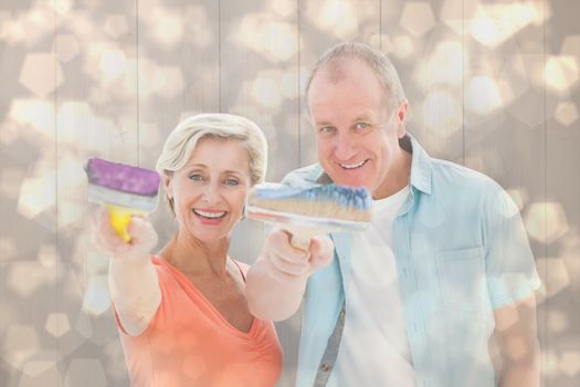 Happy older couple holding paintbrushes against light glowing dots design pattern