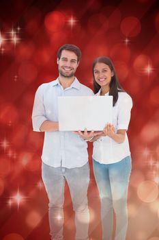 Attractive young couple holding their laptop against light design shimmering on red