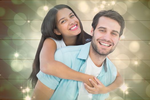 Happy casual man giving pretty girlfriend piggy back against light design shimmering on green